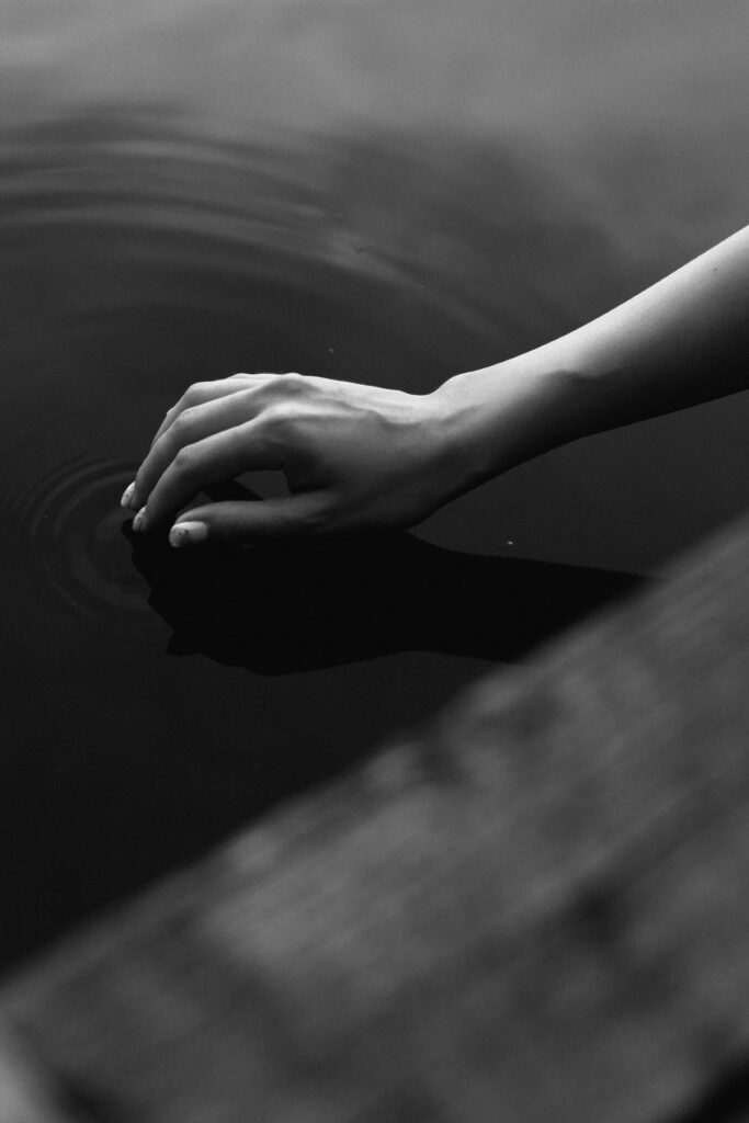 A serene black and white photograph of a hand touchwater, creating ripples.